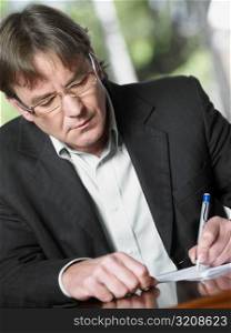 Close-up of a mature man writing on a sheet of paper