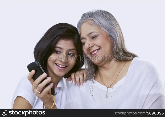 Close-up of a mature woman and her granddaughter looking at a mobile phone and smiling