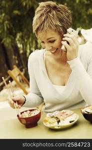 Close-up of a mature woman eating with chopsticks and talking on a mobile phone