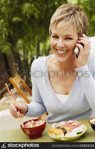 Close-up of a mature woman eating with chopsticks and talking on a mobile phone