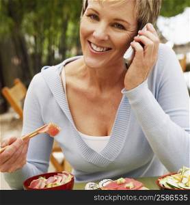 Close-up of a mature woman eating with chopsticks and talking on a mobile phone
