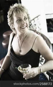 Close-up of a mature woman holding a glass of cocktail and smiling
