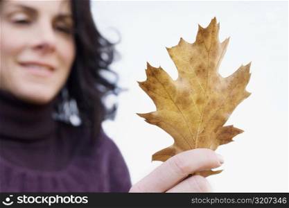 Close-up of a mature woman holding a maple leaf and smiling