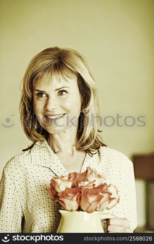 Close-up of a mature woman holding a pitcher with flowers and smiling