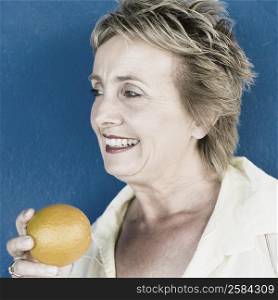 Close-up of a mature woman holding an orange and smiling