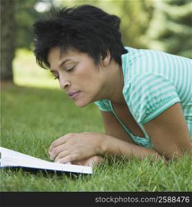 Close-up of a mature woman lying on grass and reading a book