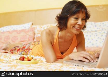 Close-up of a mature woman lying on the bed and using a laptop