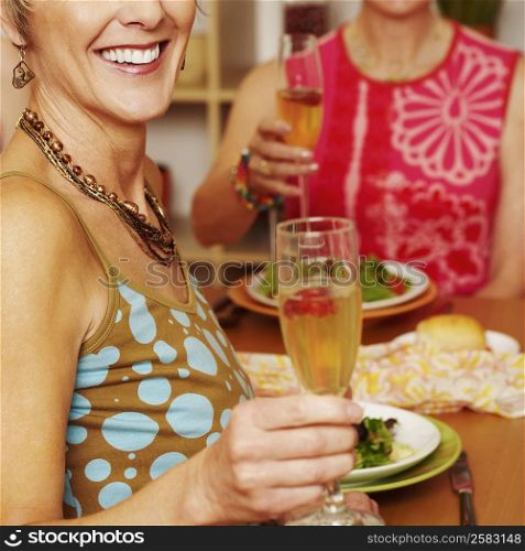 Close-up of a mature woman sitting at the dining table with her friend and holding a champagne flute