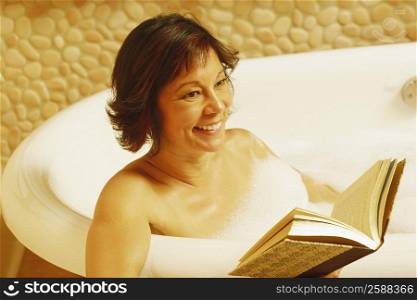 Close-up of a mature woman sitting in a bathtub and holding a book