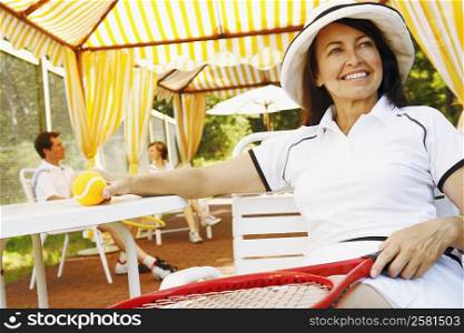 Close-up of a mature woman sitting on a chair holding a tennis ball and a tennis racket