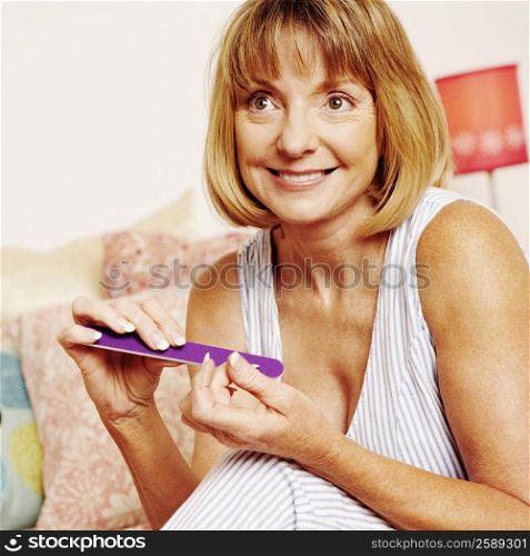 Close-up of a mature woman sitting on the bed and filing her fingernails with a nail file