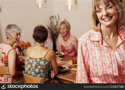 Close-up of a mature woman smiling and her friends sitting at the dining table in the background