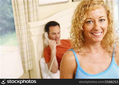 Close-up of a mature woman smiling with a mature man talking on the telephone in the background
