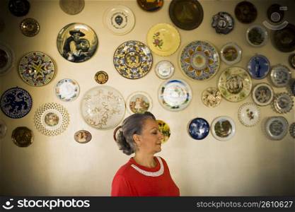 Close-up of a mature woman standing in front of a wall decorated with ceramics