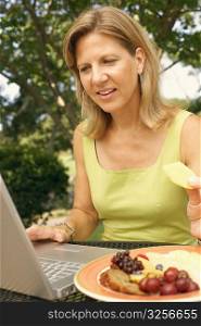 Close-up of a mature woman using a laptop and eating fruit salad
