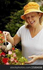 Close-up of a mature woman watering plants and smiling