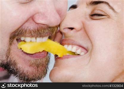 Close-up of a mid adult couple biting into a slice of fruit together