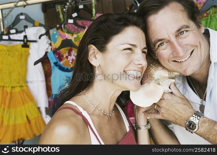 Close-up of a mid adult couple listening to a conch shell and smiling