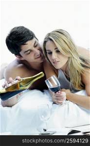 Close-up of a mid adult couple lying on the bed and holding a bottle and a glass of wine