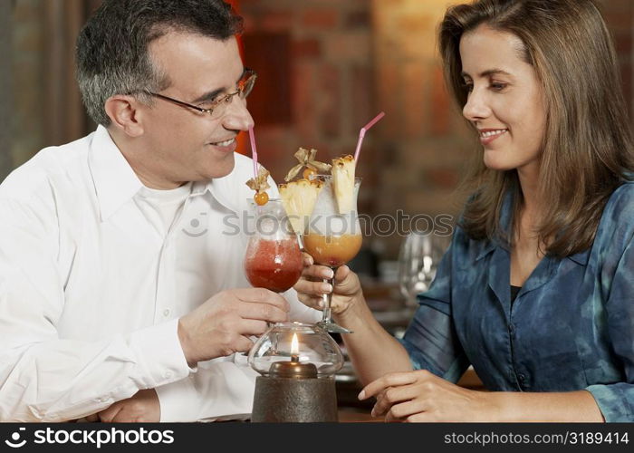 Close-up of a mid adult couple sitting in a restaurant and toasting glasses of pina colada