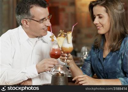 Close-up of a mid adult couple sitting in a restaurant and toasting glasses of pina colada