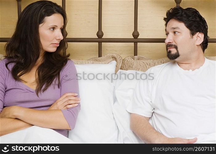 Close-up of a mid adult couple sitting on the bed and looking at each other