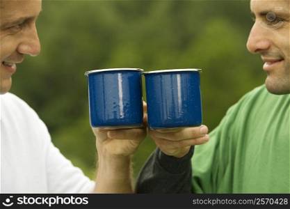 Close-up of a mid adult man and a mature man toasting with mugs