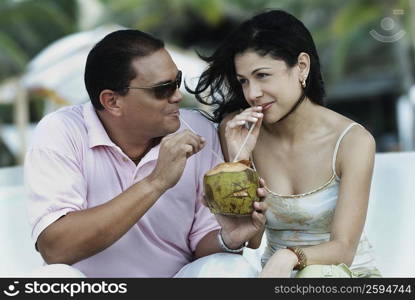 Close-up of a mid adult man and a young woman drinking coconut water