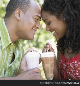 Close-up of a mid adult man and a young woman holding glasses of milkshake