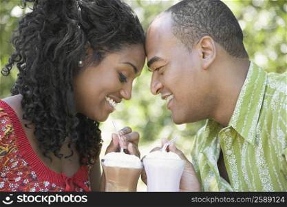 Close-up of a mid adult man and a young woman holding glasses of milkshake