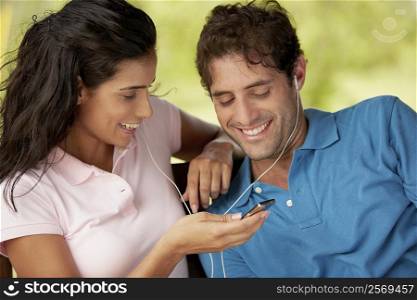 Close-up of a mid adult man and a young woman listening to an MP3 player