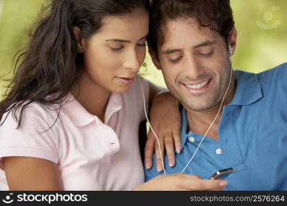 Close-up of a mid adult man and a young woman listening to an MP3 player