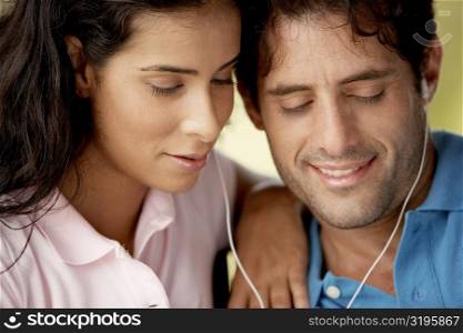 Close-up of a mid adult man and a young woman listening to music through headphones
