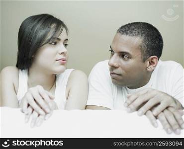 Close-up of a mid adult man and a young woman lying on the bed and looking at each other