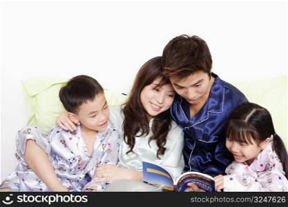 Close-up of a mid adult man and a young woman with their children reading a book on the bed