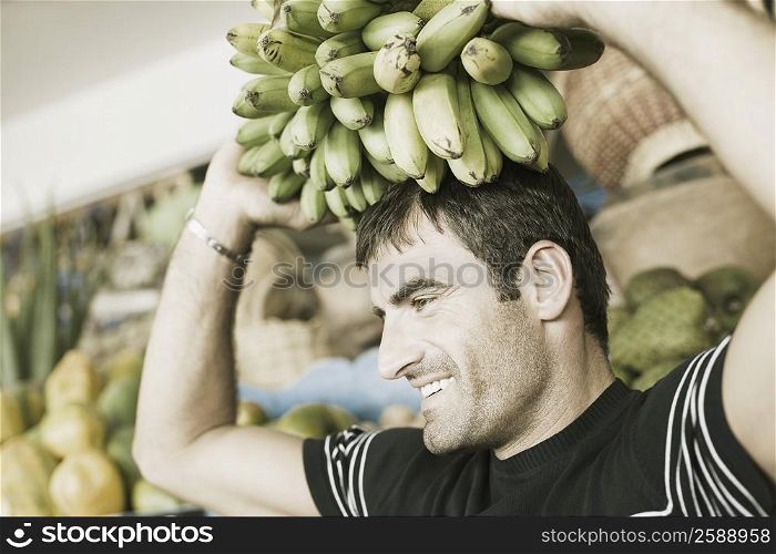 Close-up of a mid adult man carrying a bunch of bananas on his head
