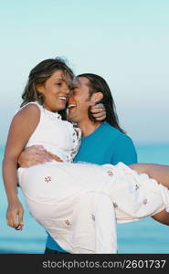 Close-up of a mid adult man carrying a young woman on the beach