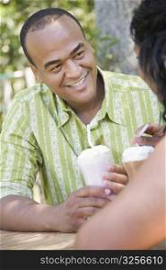 Close-up of a mid adult man drinking milkshake with a drinking straw and his girlfriend sitting in front of him