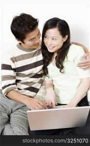 Close-up of a mid adult man embracing a young woman using a laptop