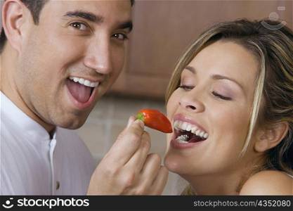 Close-up of a mid adult man feeding a red chili pepper to a young woman
