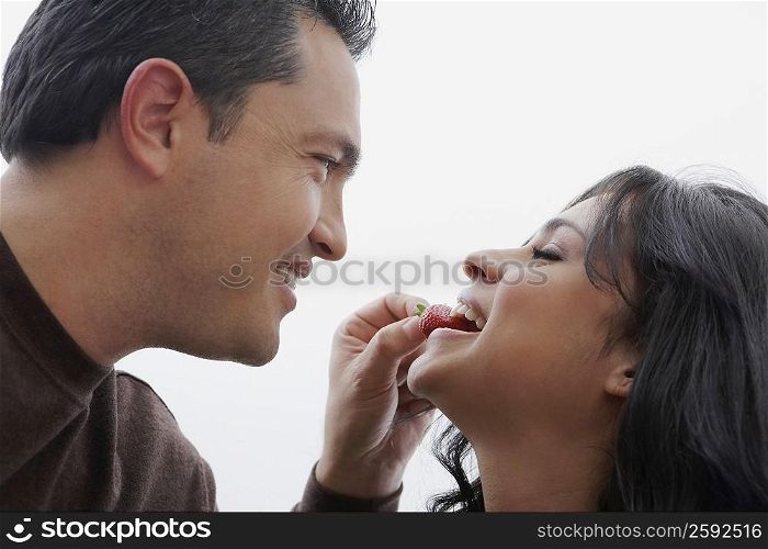 Close-up of a mid adult man feeding a strawberry to a young woman