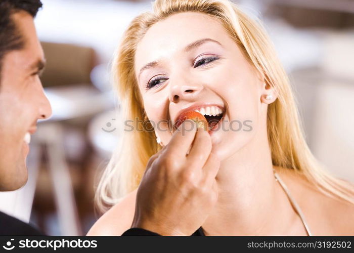 Close-up of a mid adult man feeding a young woman a strawberry