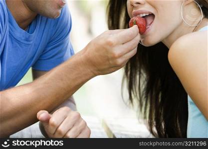 Close-up of a mid adult man feeding a young woman a strawberry