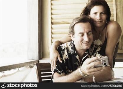 Close-up of a mid adult man holding a digital camera with a mid adult woman beside him