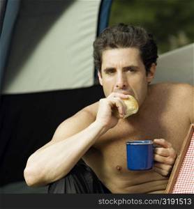 Close-up of a mid adult man holding a mug eating a piece of bread