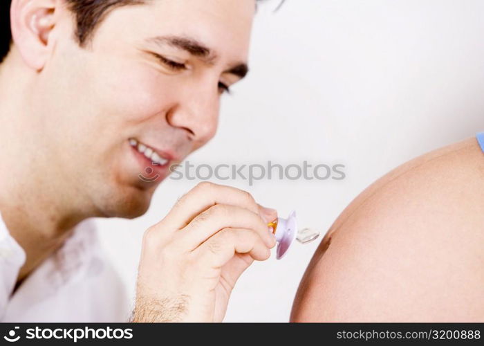 Close-up of a mid adult man holding a pacifier and touching it to a pregnant woman&acute;s abdomen