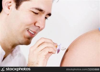 Close-up of a mid adult man holding a pacifier and touching it to a pregnant woman&acute;s abdomen