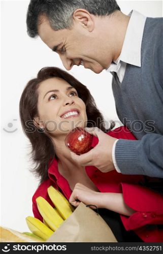 Close-up of a mid adult man holding an apple with a mid adult woman holding a shopping bag beside her