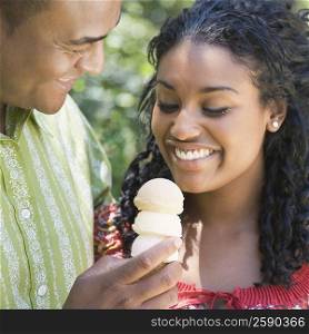 Close-up of a mid adult man holding an ice cream and a young woman eating it