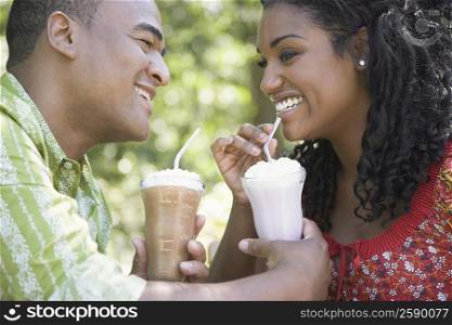 Close-up of a mid adult man holding glasses of milkshake and young woman drinking it